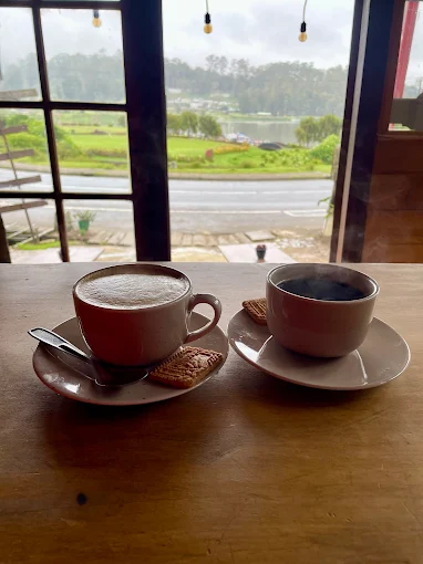 Two coffees on a wooden table by the café window, looking out over the lake